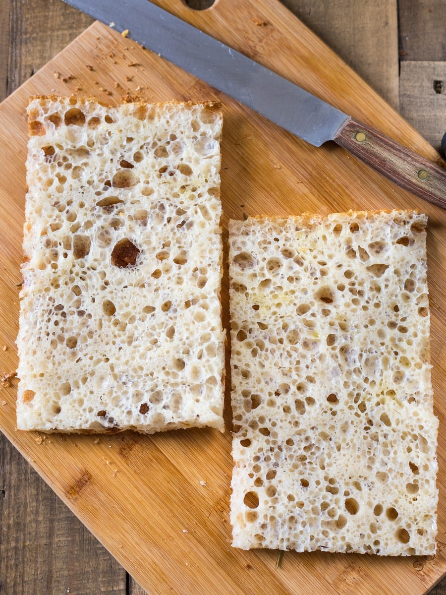 A piece of focaccia sliced in half to be filled with tomato and mozzarella to make caprese focaccia sandwich.