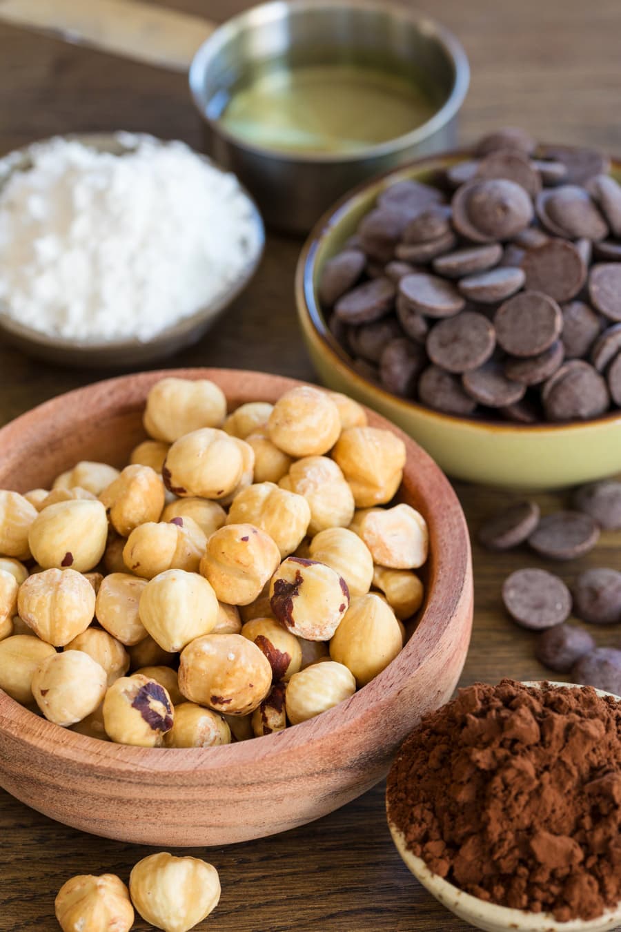 Small bowls containing hazelnuts, dark chocolate chips, cocoa powder, powdered sugar and vegetable oil.