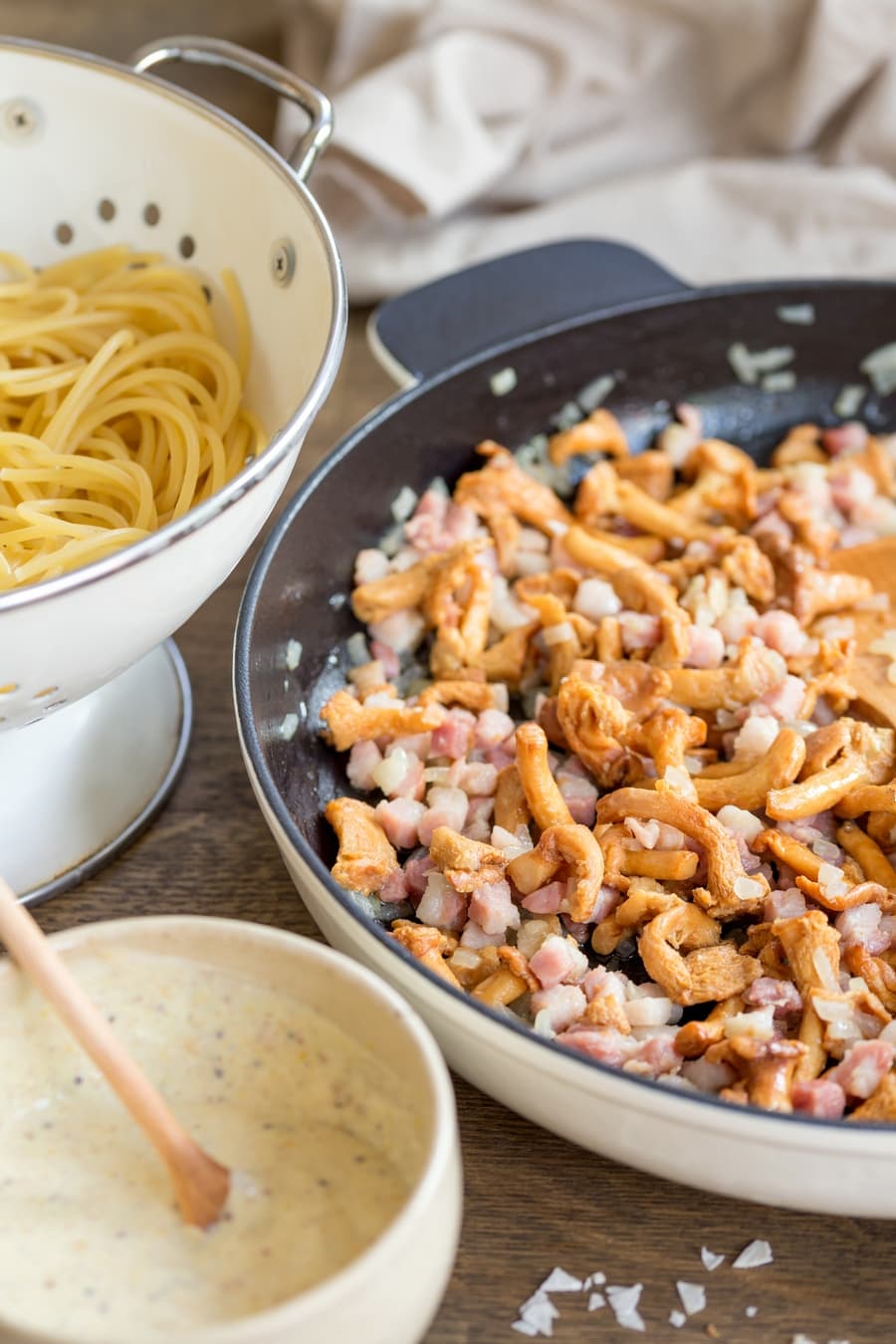Boiled spaghetti in a colander, sautéed mushromms and bacon in a skillet and creamy mustard sauce in a bowl.
