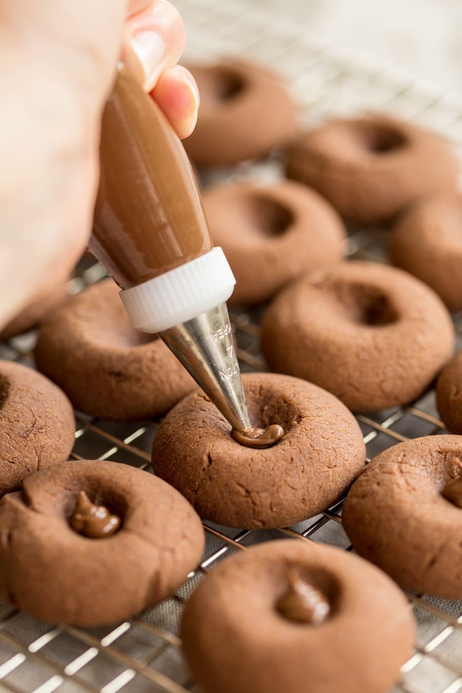 Piping Nutella in the hole of nutellotti thumbprint cookies.