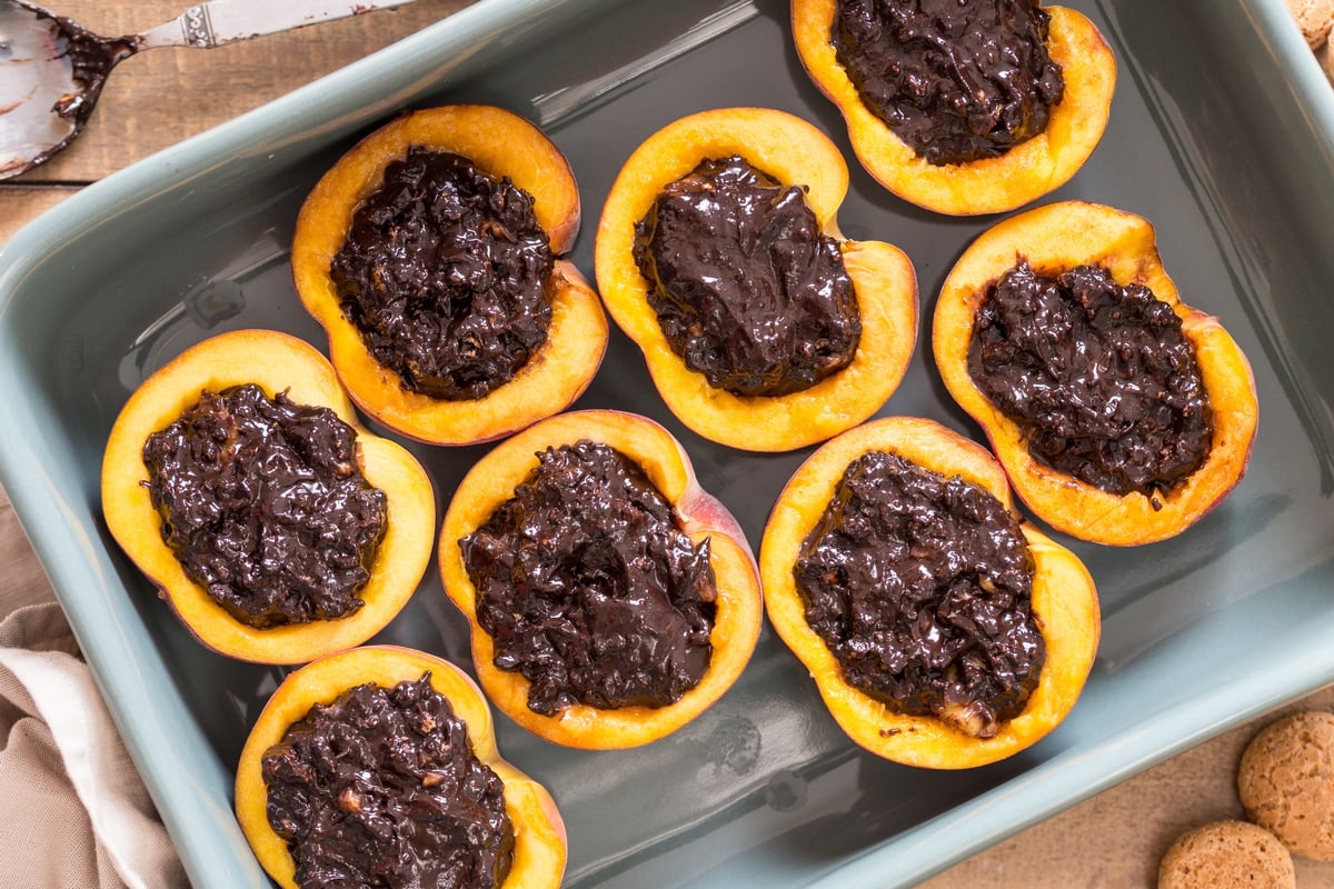 Halved peaches with amaretti filling in an oven dish.