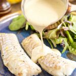 Pouring lemon pepper cream sauce over baked cod fillets.