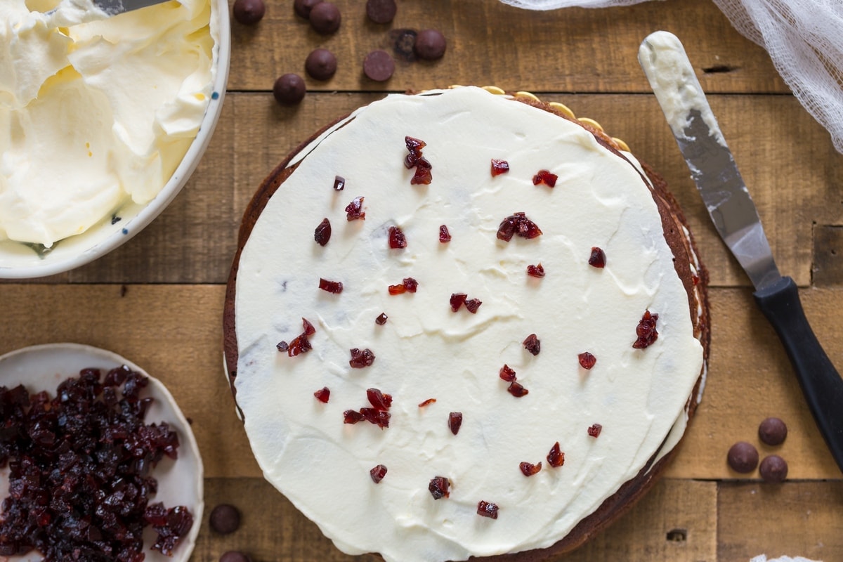 Assembling the Black Forest cherry cake with layers of whipped cream and minced sour cherries in syrup.