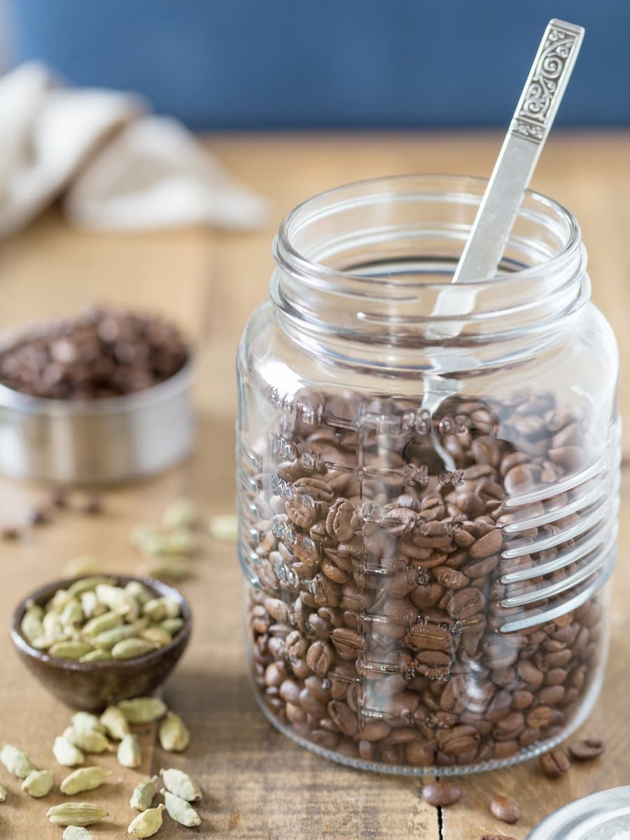 Mason jar withh coffee beans in, cardamom pods in a small bowl beside.