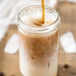 Pouring coffee into milk glass to make cardamom cold brew iced latte.