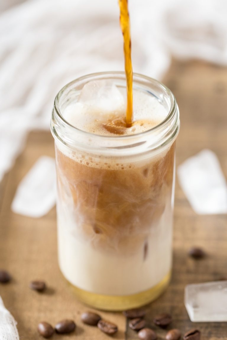 Pouring coffee into milk glass to make cardamom cold brew iced latte.