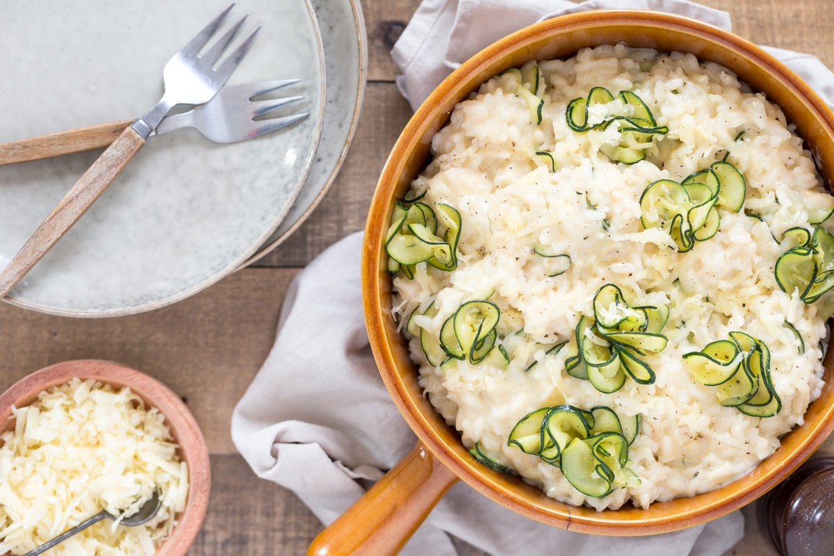 Overhead view of zucchini cheddar risotto, serving plates on the side.