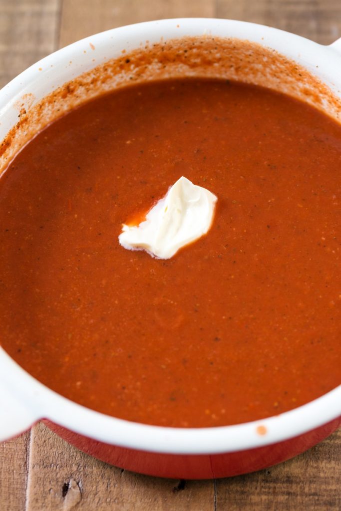 A dollop of cream on zupa pomidorowa in a pot.