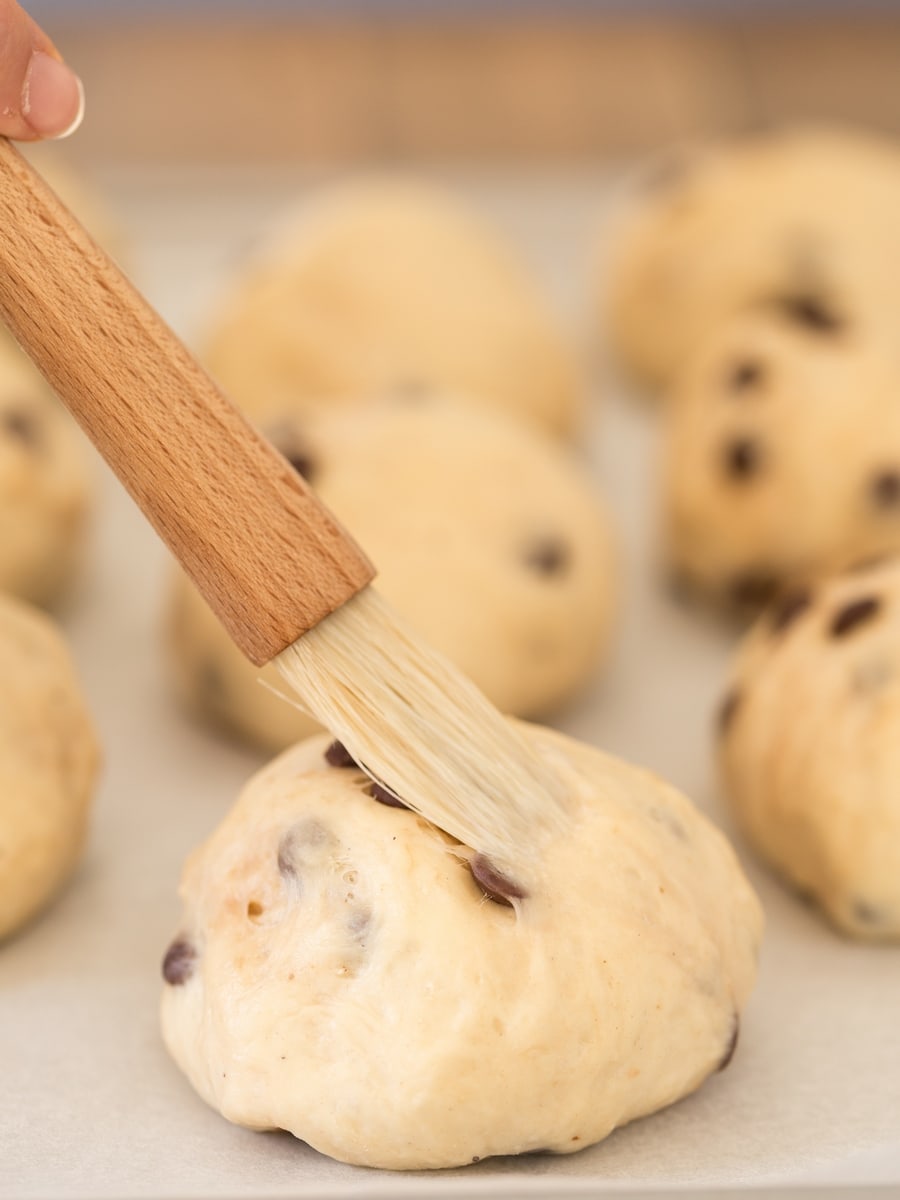 Brushing milk over unbaked wheat bun.