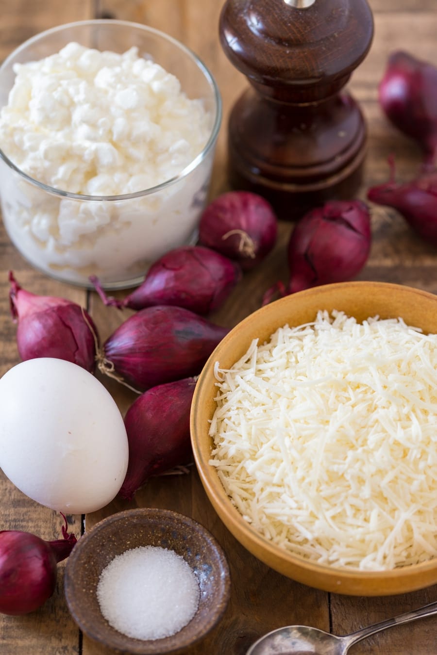 Grated parmesan in a bowl, an egg, small bowl with salt, pearl onions and cottage cheese in another bowl.