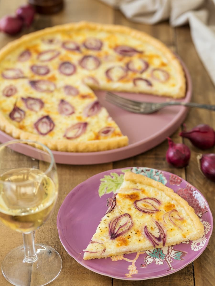 Slice of onion cottage cheese tart, glass of white wine.
