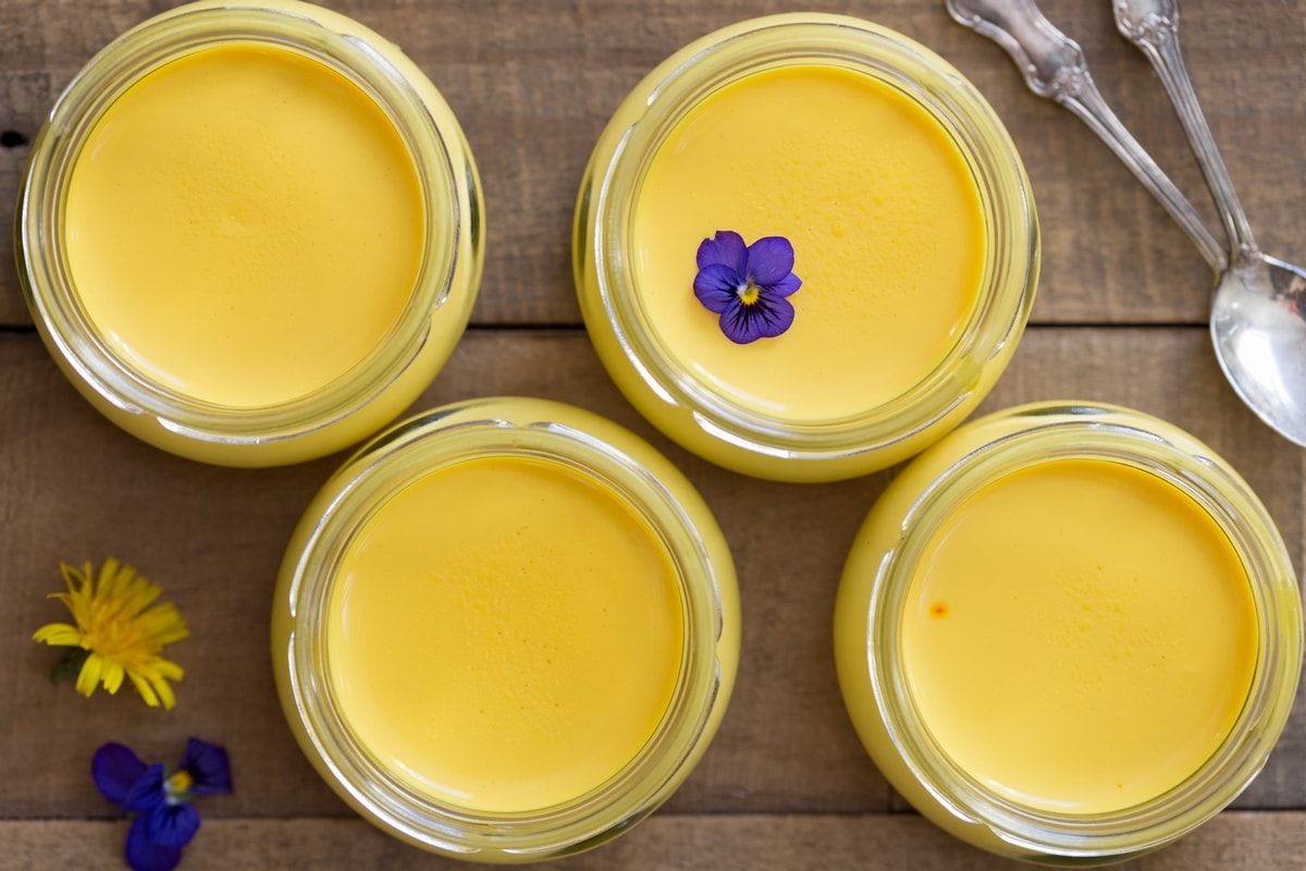 Small glass jars with saffron panna cotta on a wooden table.