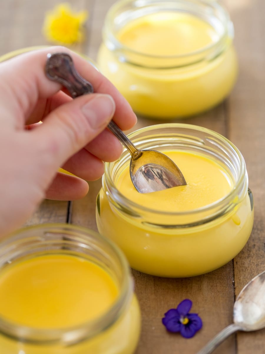 Hand with teaspoon digging into portion of saffron panna cotta.