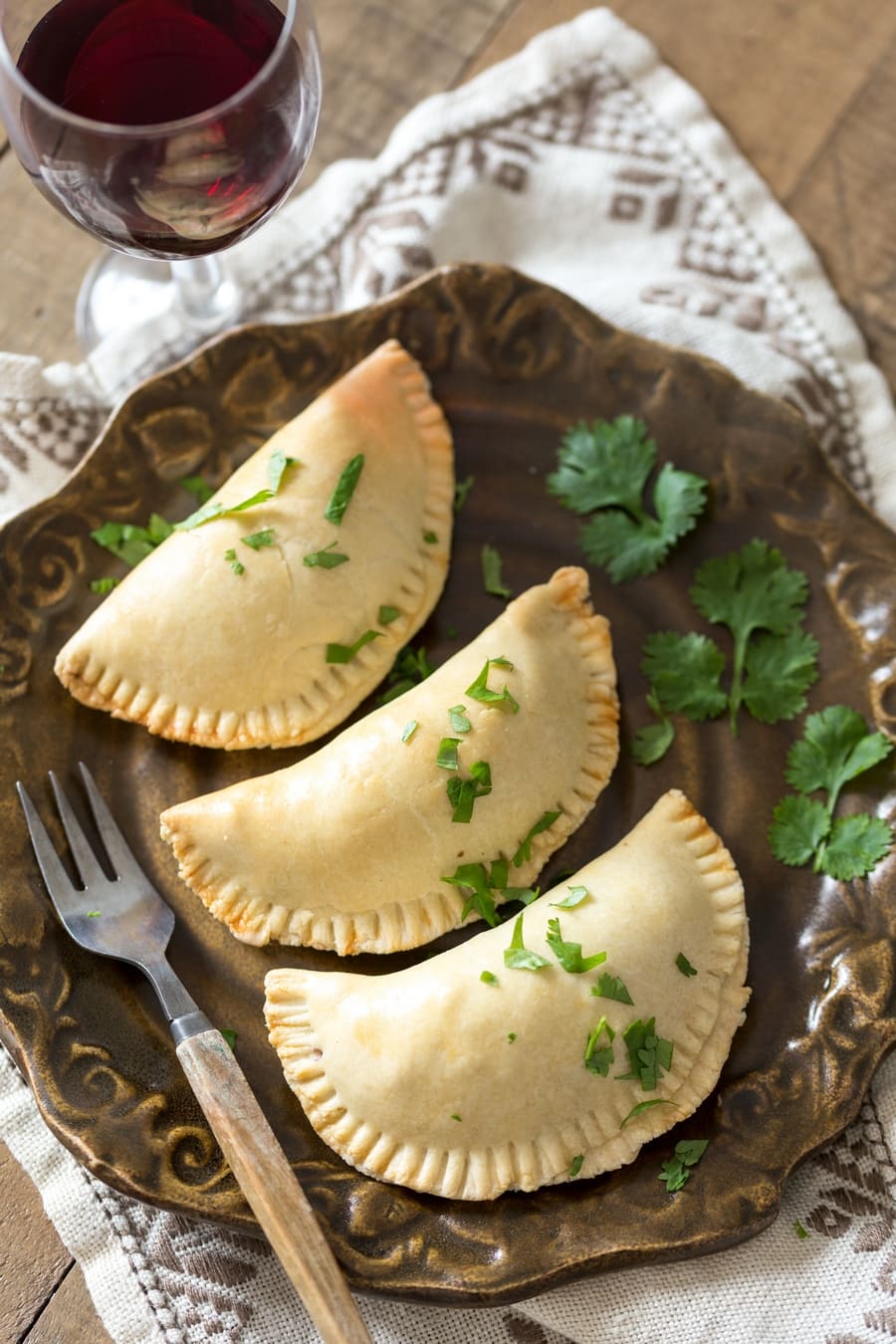 Veggie empanadas on a brown plate, decorated with cilantro.