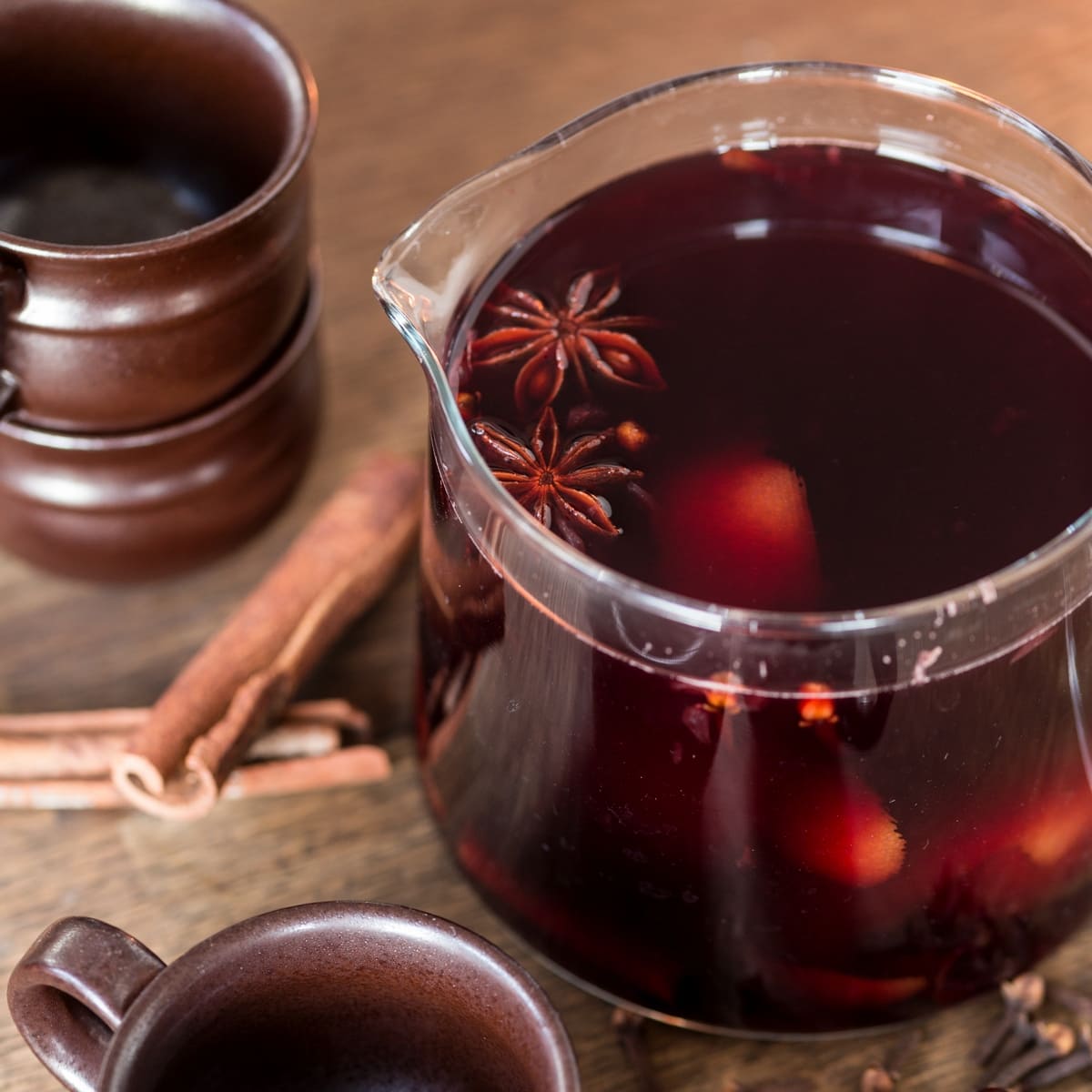 Glass jug filled with mulled wine and spices, serving mugs next to it.