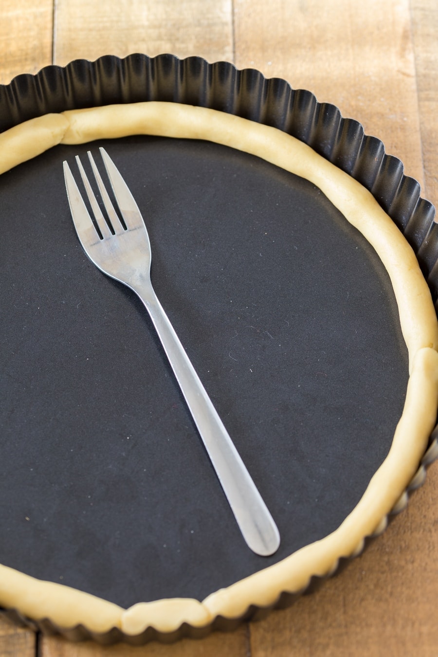 Tart pan with roll of shortcrust pastry on the edges, fork in the middle.