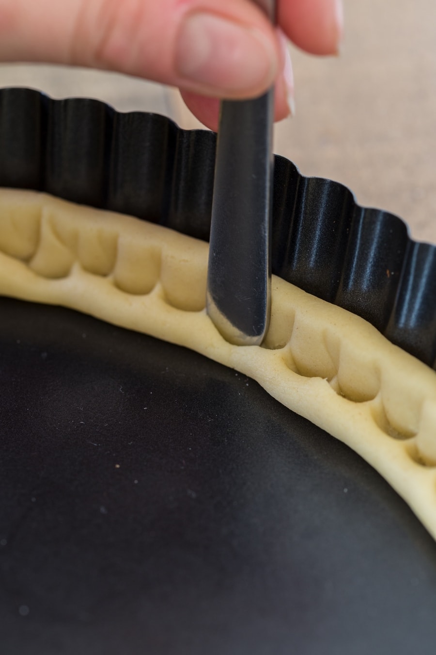Pressing shortcrust pastry to tart pan sides with the handle of a fork.