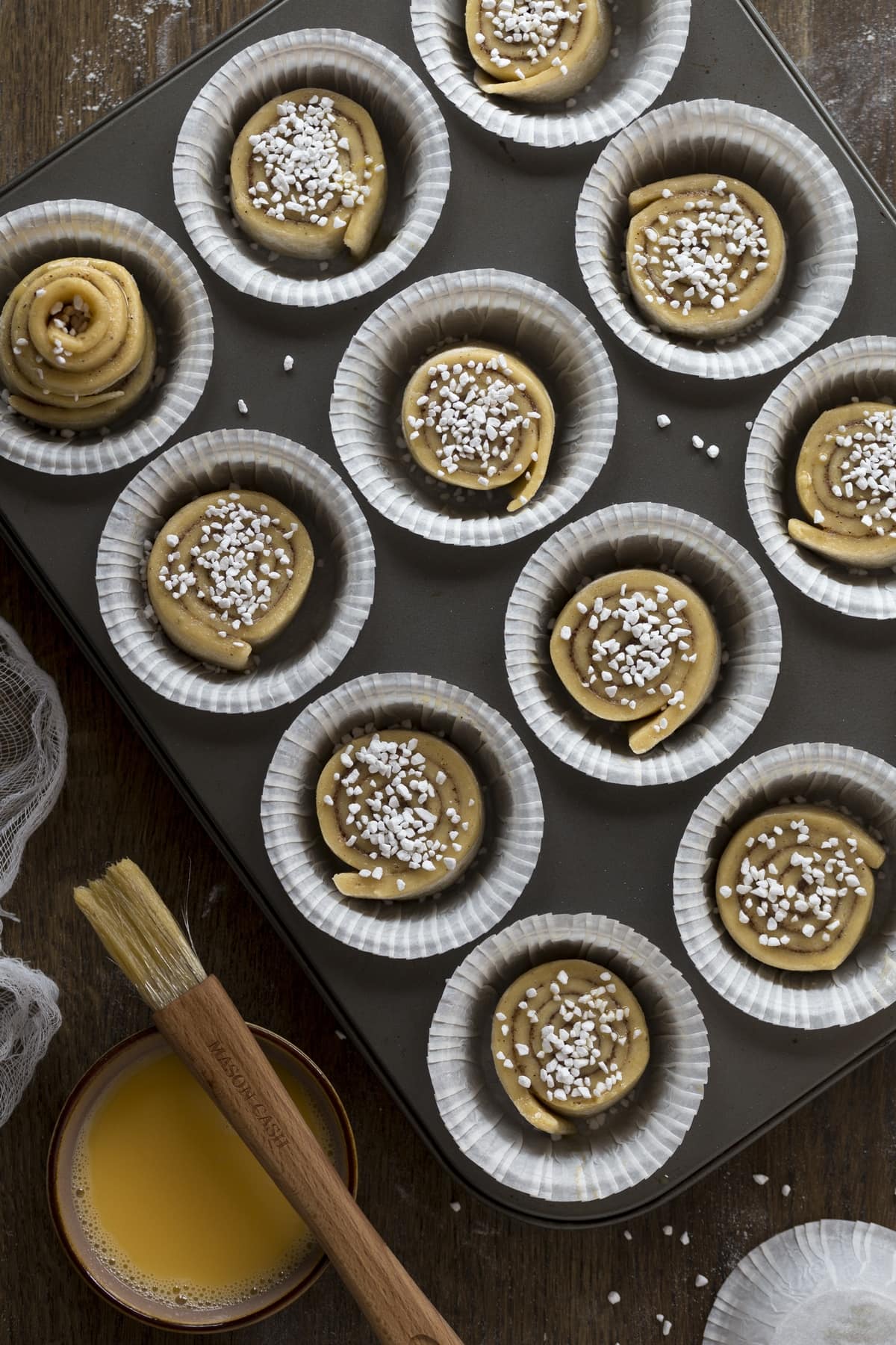 Eggwash and pearl sugar added to unbaked muffin tin kanelbulle.