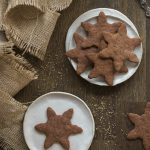 Overhead shot of gingerbread cookies on small white plates on a wooden table.