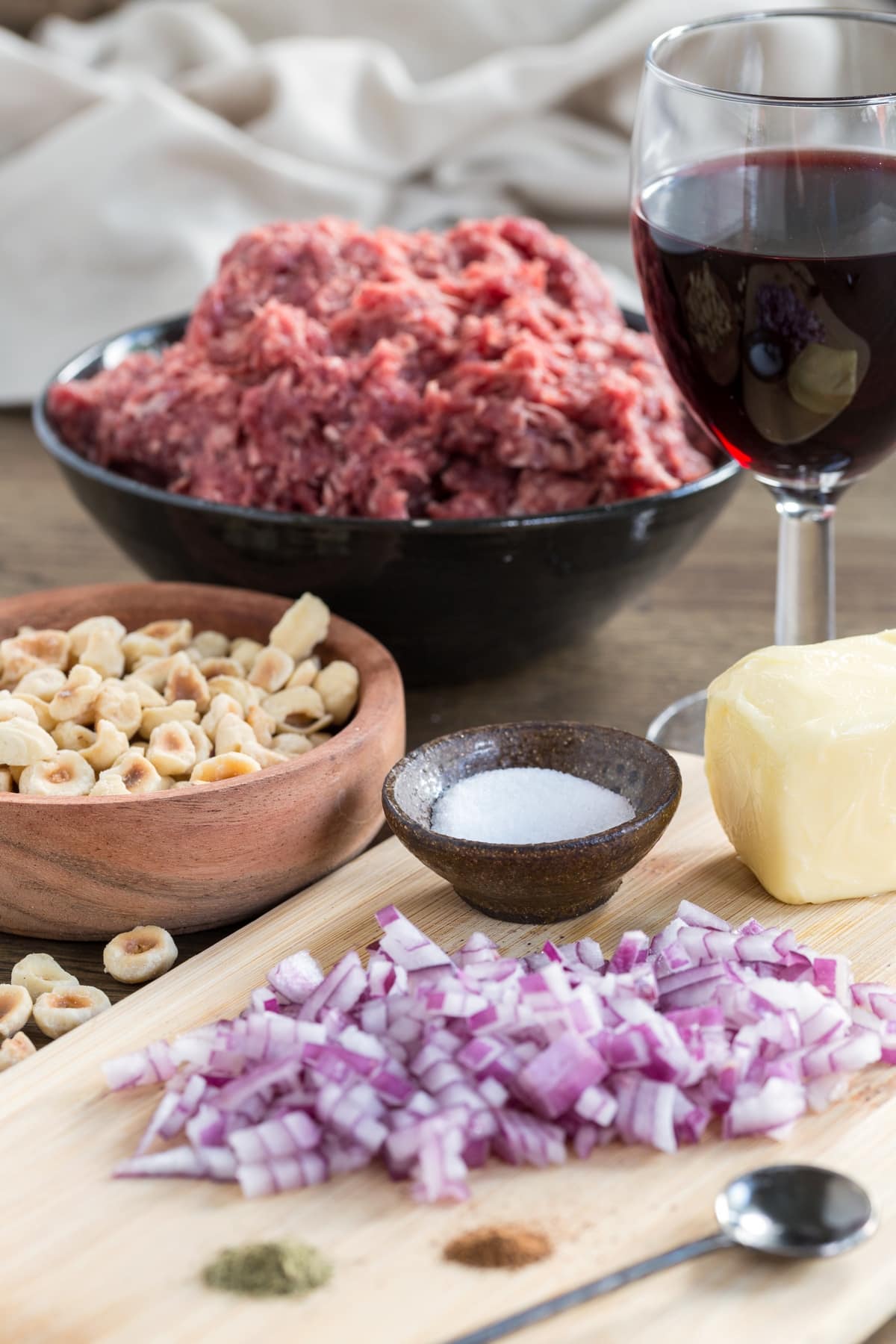Chopped red onion on a cutting board, salt, butter, hazelnuts and ground venison in the background.