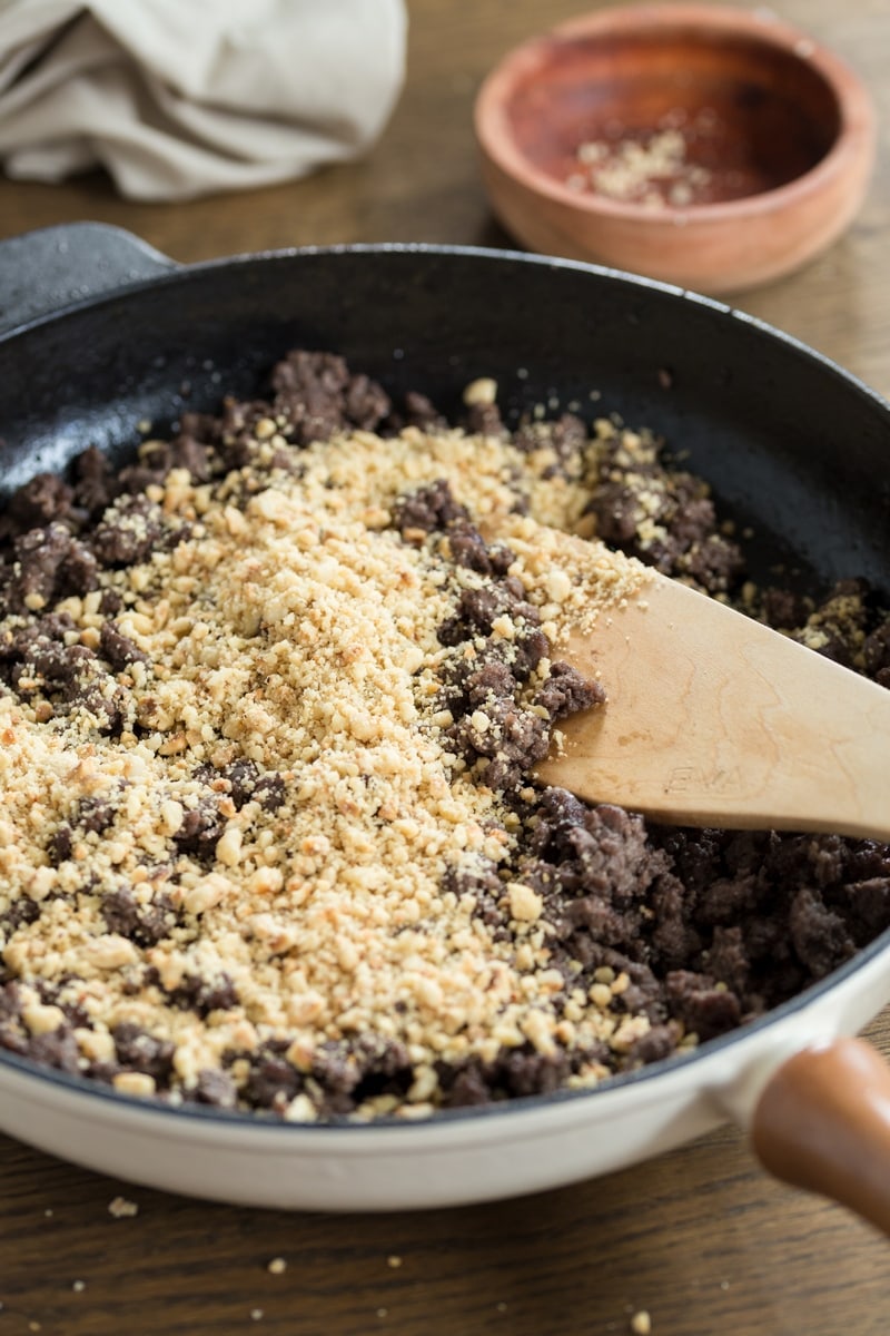 Ground hazelnuts added to ground venison in a skillet.