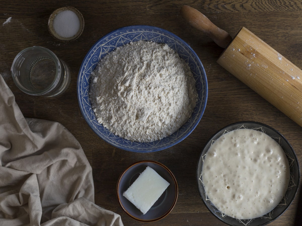 Bowls containing flour, lard, salt and sourdough starter on a table.