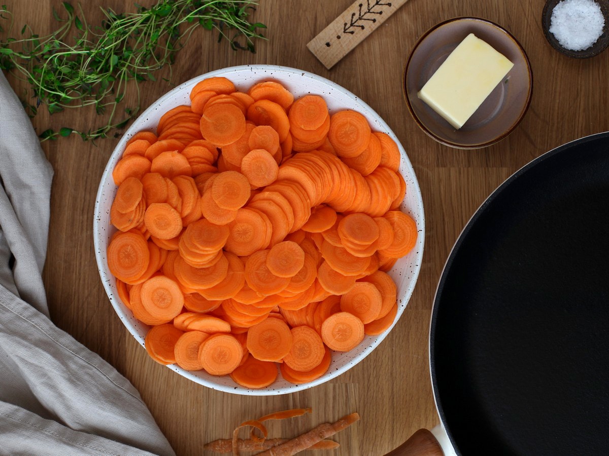 Thinly sliced raw carrots in a white bowl.