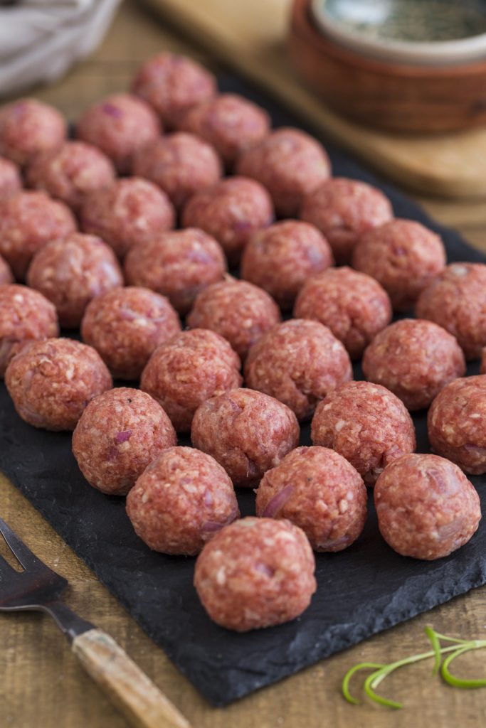 Raw meatballs on a black plate.