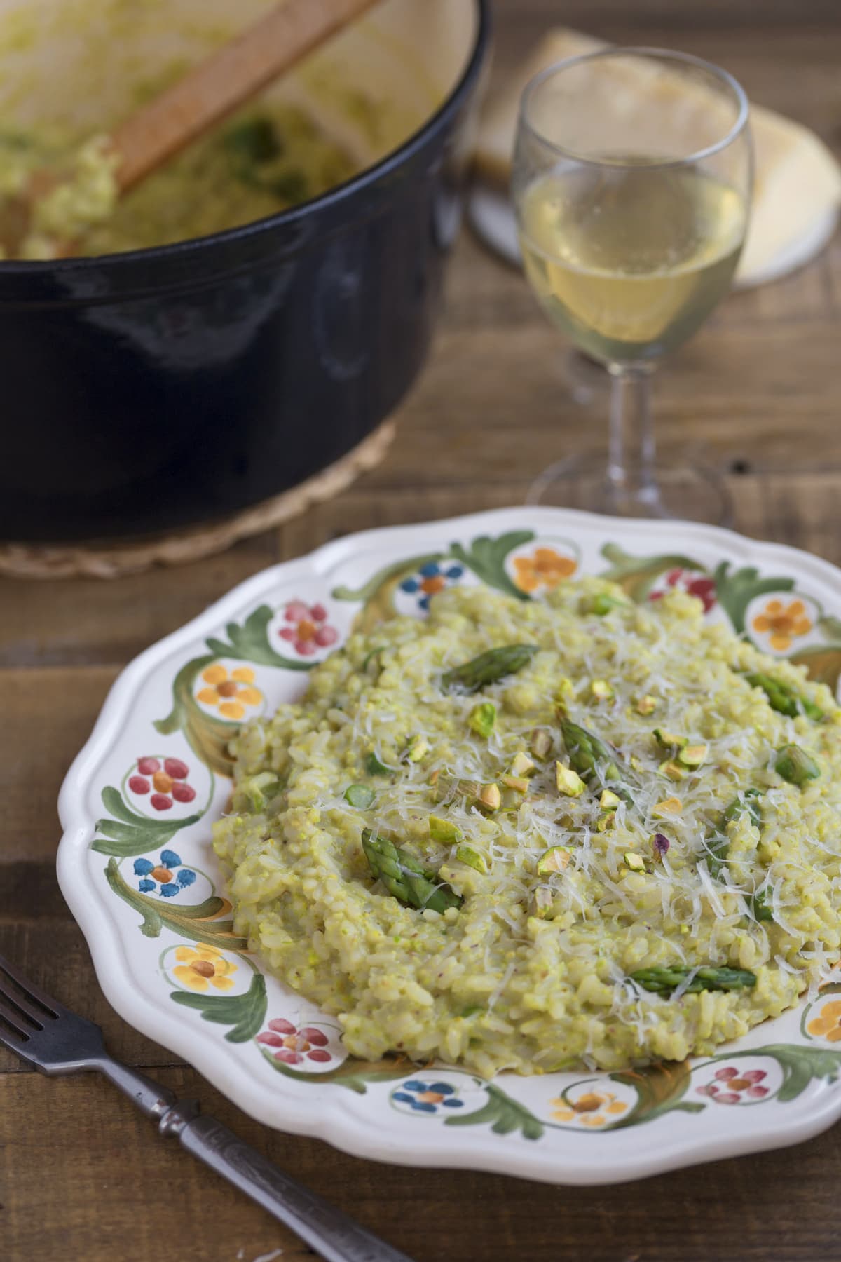 A plate of asparagus risotto nest to a Dutch oven and a glass of white wine.