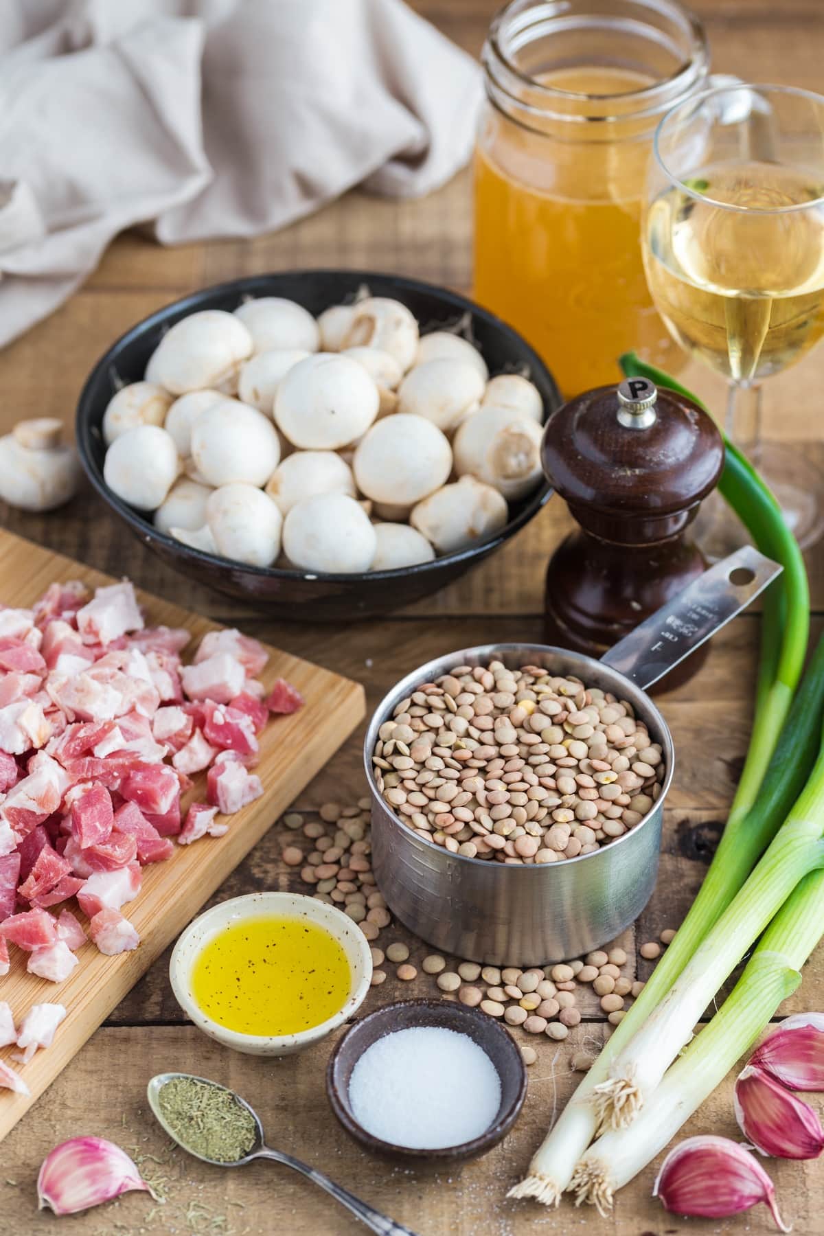 A cup of dried brown lentils surrounded by diced bacon, mushrooms, spring onions and condiments.