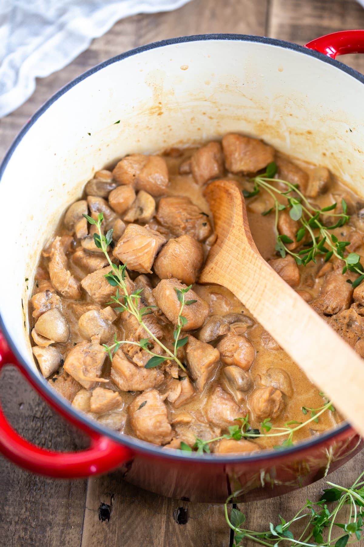 Cream cheese chicken and mushrooms stew in a red Dutch oven pot.