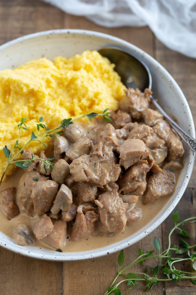 Chicken stew and polenta in a white bowl.
