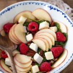 Apple brie and raspberry salad in a white bowl.