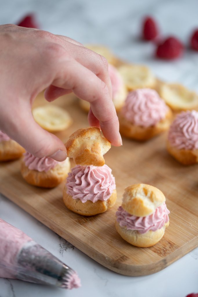 Choux pastry puffs filled with raspberry cream, hand placing lid on top of filling.