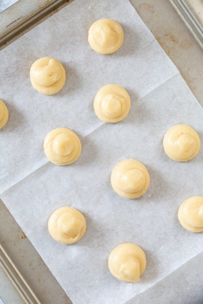 Choux pastry puffs piped onto baking paper about to be baked.