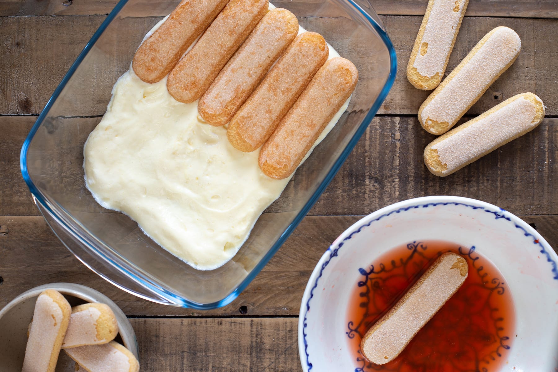 Creating a layer of soaked ladyfinger biscuits.