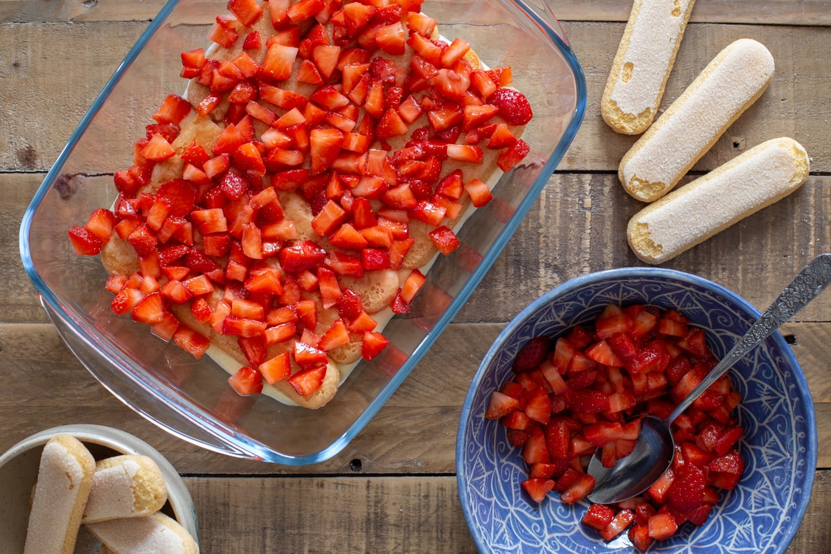 Adding a layer of diced strawberries over the biscuit layer.