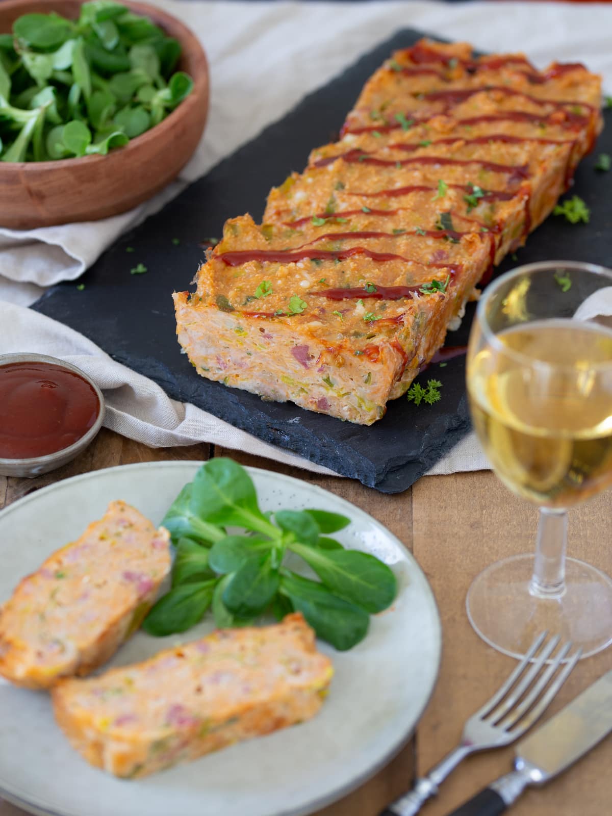 Chicken meatloaf with bacon and leeks on a black serving plate.