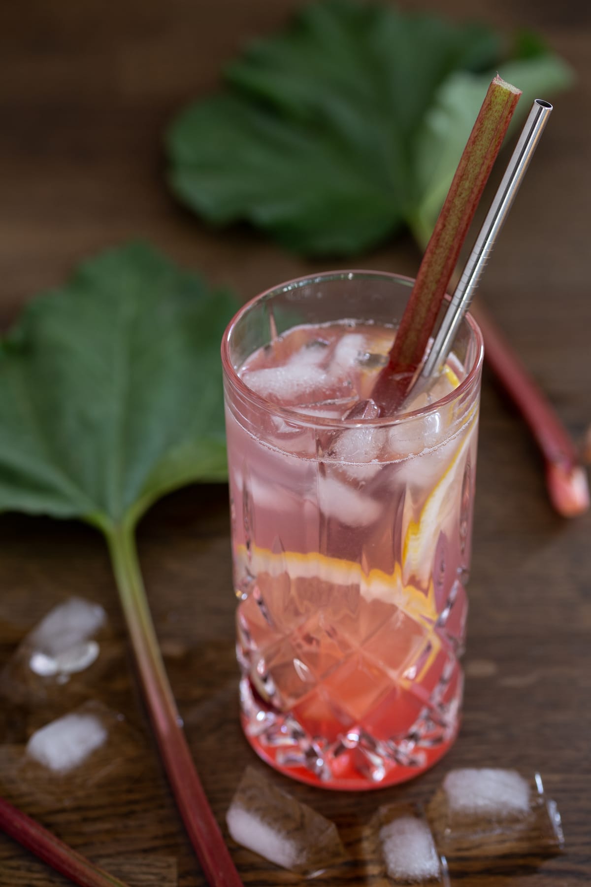 A glass of rhubarb gin tonic with rhubarb leaves next to it.