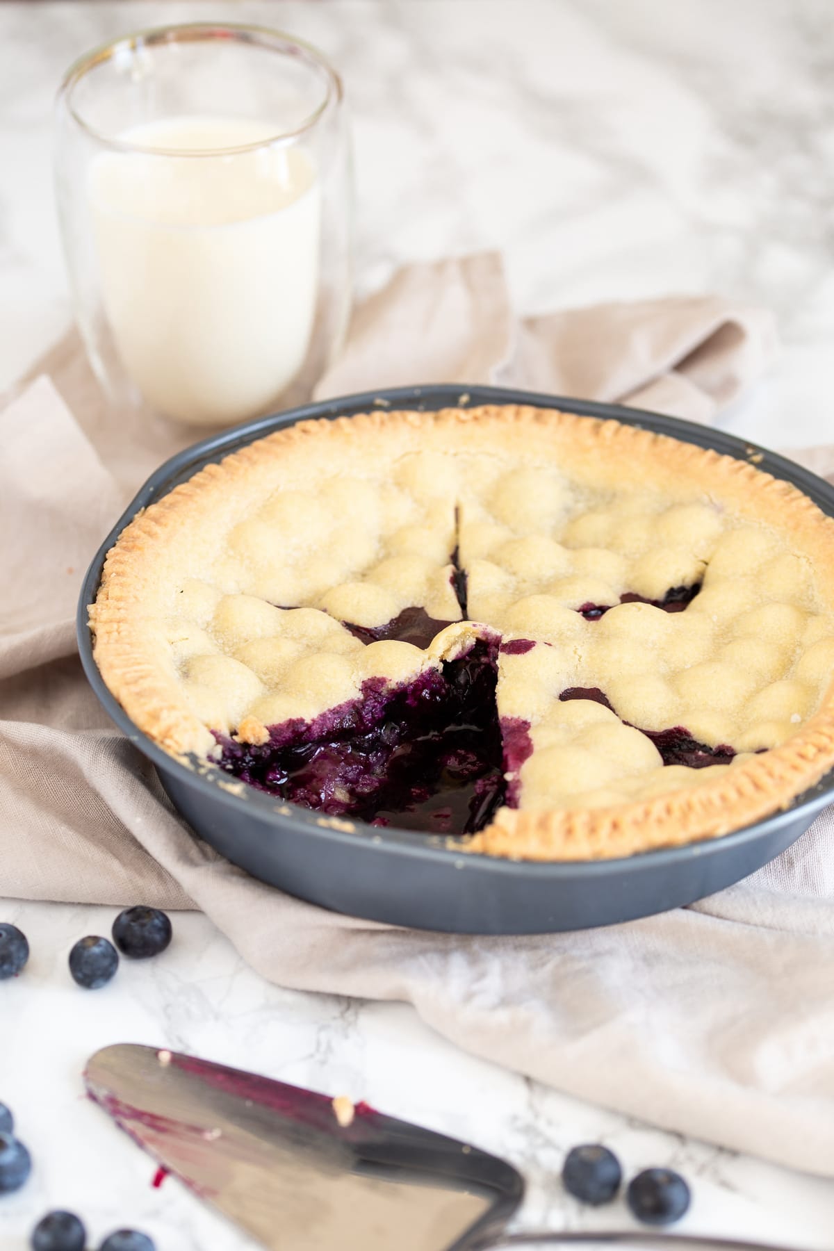 Blueberry pie, sliced. A glass of milk in the background.