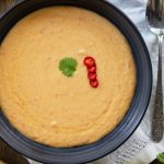 REd lentil soup with coconut cream, lime and chili served in a blue bowl.