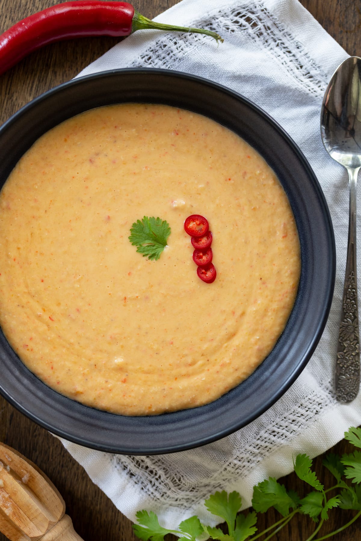 REd lentil soup with coconut cream, lime and chili served in a blue bowl.