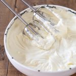 Electric mixer whisks resting inside the bowl of frosting.