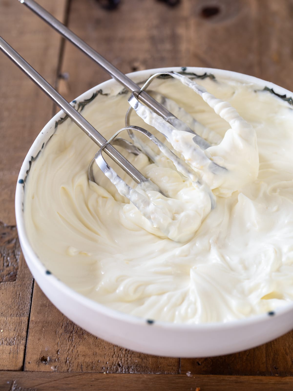 Electric mixer whisks resting inside the bowl of frosting.