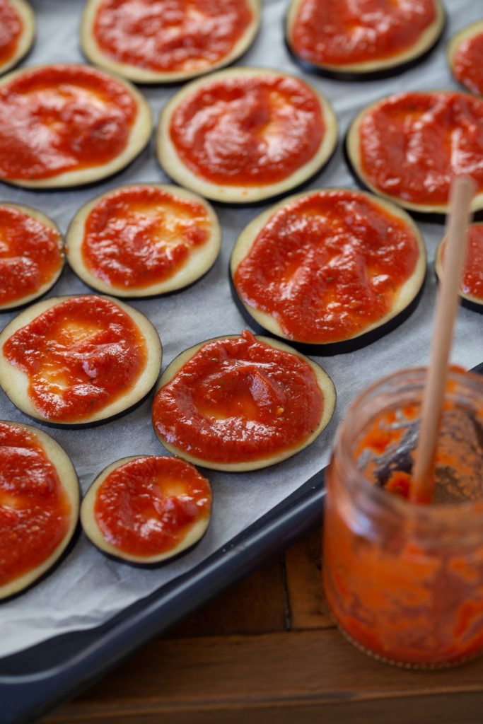 Spreading tomato sauce on eggplant slices.