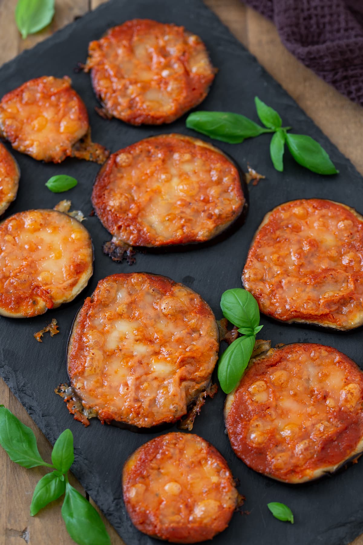 Baked eggplant pizzette on a black tray.