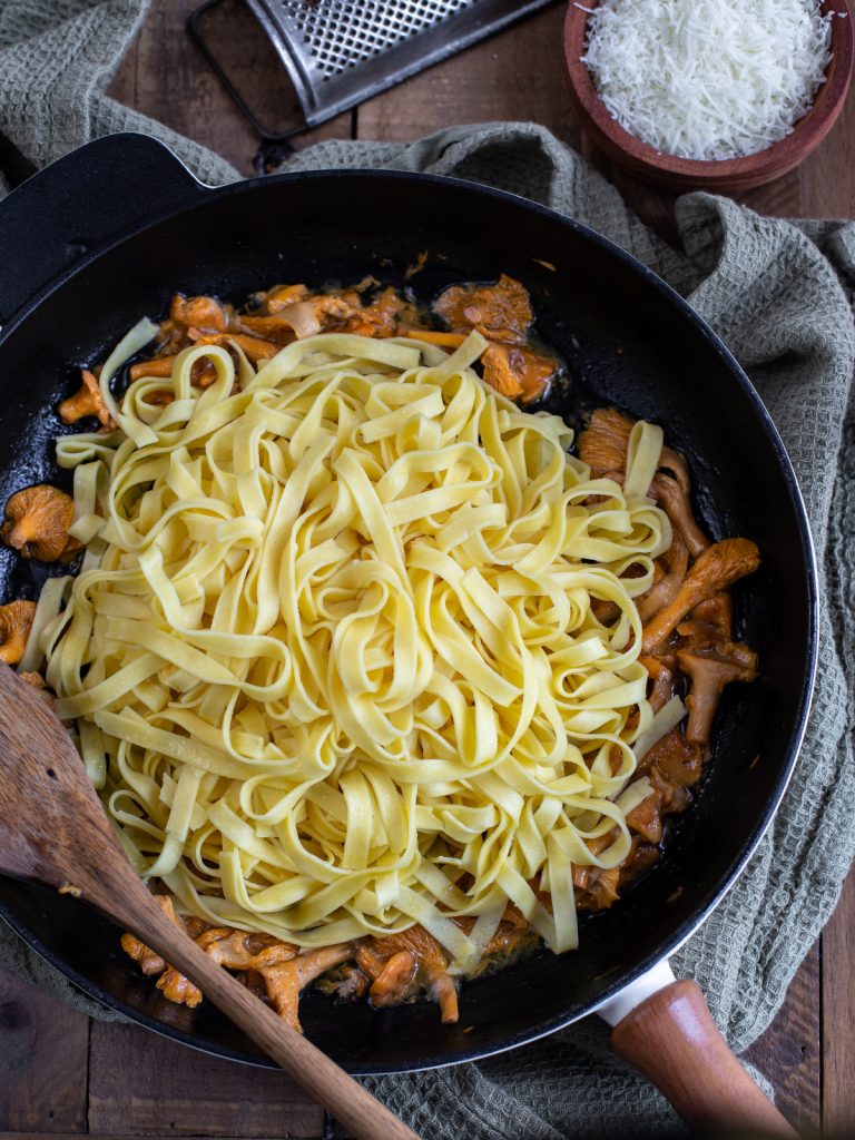 Adding cooked pasta to the mushroom sauce.