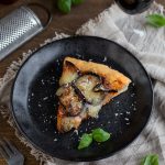 Eggplant parmesan pizza slice on a black plate.