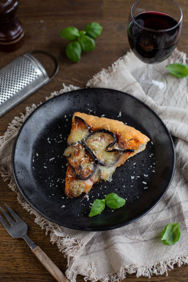 Eggplant parmesan pizza slice on a black plate.