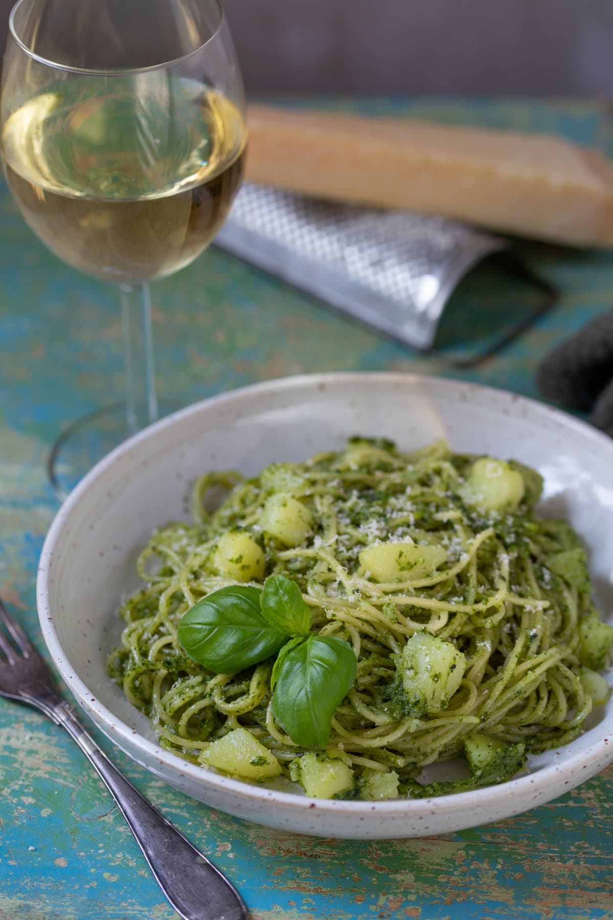 A portion of pesto pasta with potatoes in a white bowl.